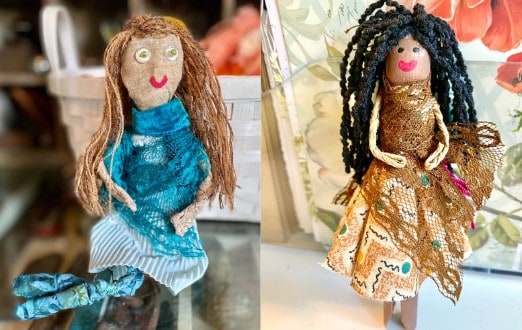 A rag doll with red hair wearing a blue dress and a clothespin doll with black hair wearing a brown dress.