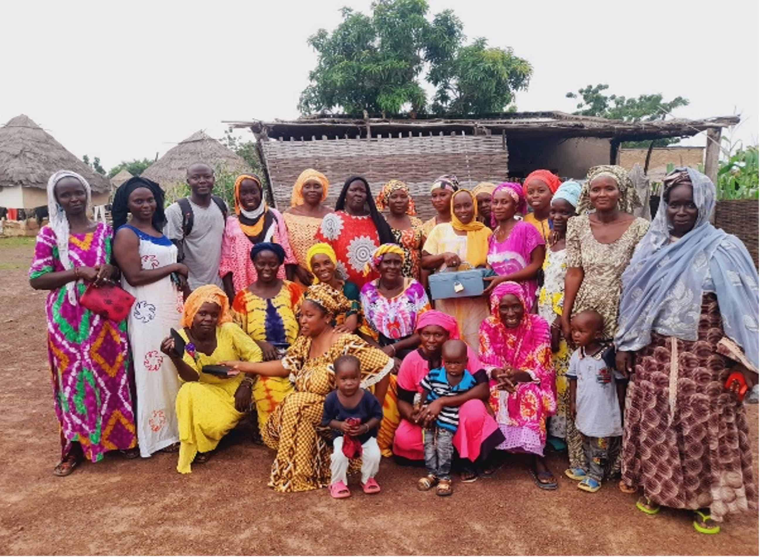 Group of girls, women, children and facilitators in colorful clothing standing and sitting together in a rural village in Senegal, celebrating the success of Plan International's Girls Learn & Thrive program.