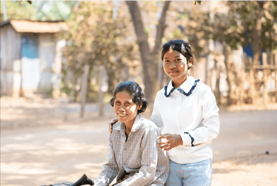 In Cambodia, a grandmother and her granddaughter smile together in an outdoor village setting.