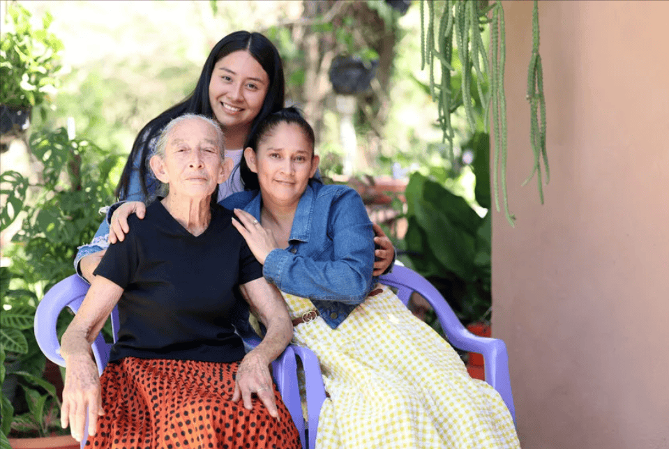 Three generations of women from El Salvador pose together outside, smiling warmly.
