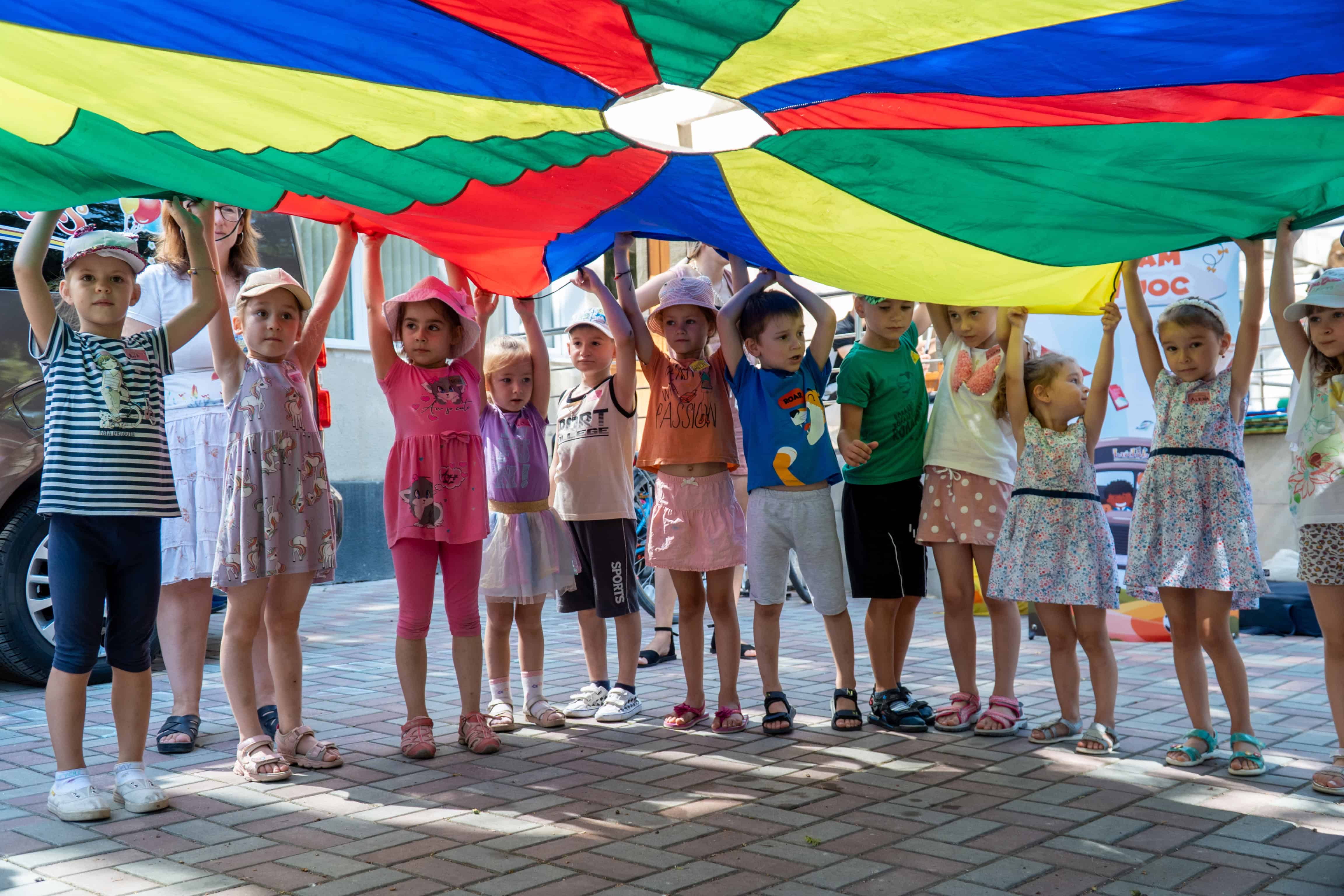 Children in Moldova stand in a circle holding up a colorful parachute during a visit from the Ludobus, Plan’s mobile play bus that offers games, books and psychosocial support for refugee and host community families.