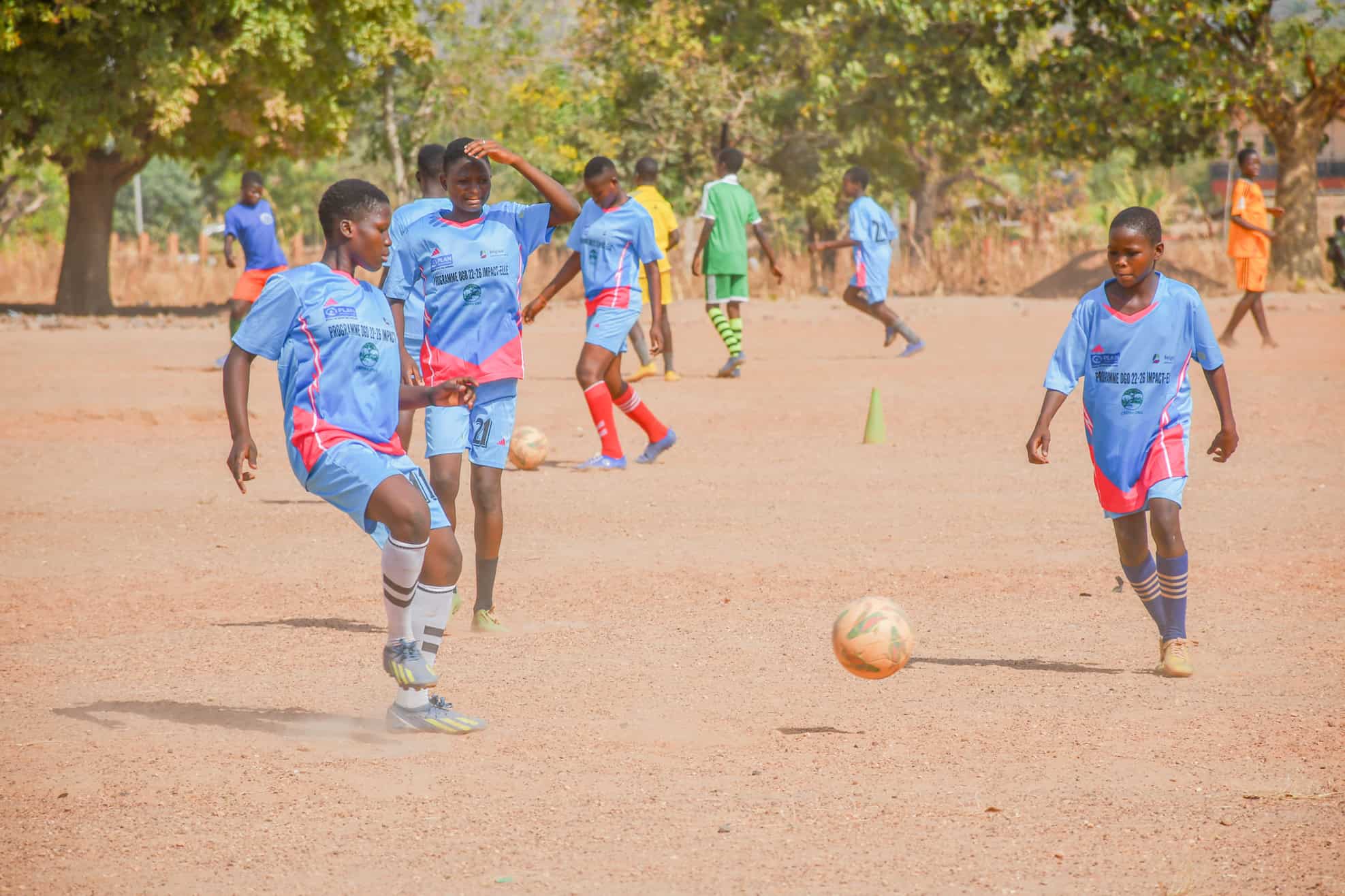 Girls in Atacora, Benin, play football in matching uniforms on a dirt field as part of Plan International’s Impact-Elle project, which uses sport to promote gender equality and leadership.
