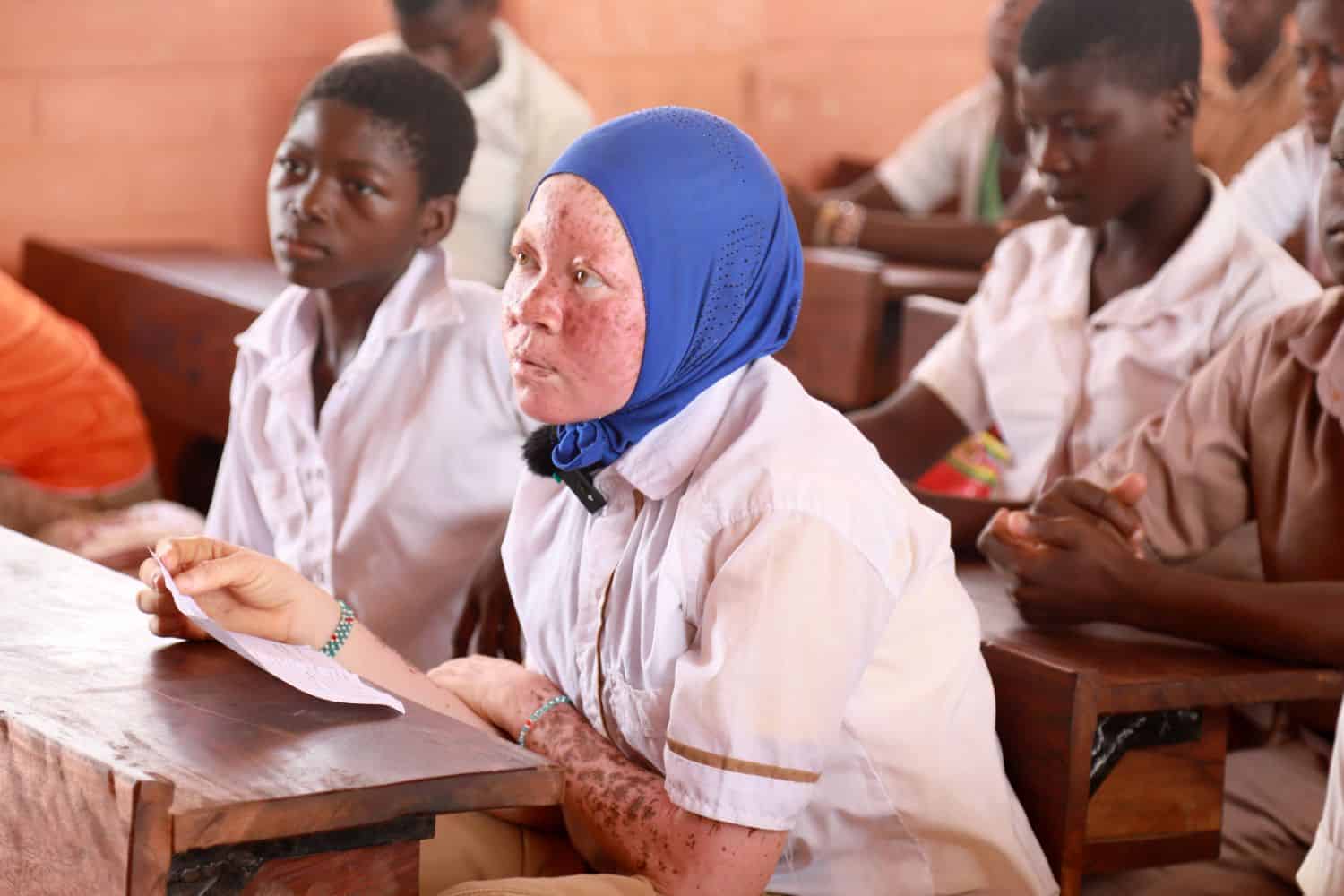 Rachidatou, a student with albinism, listens attentively in class in northern Togo while holding a piece of paper.