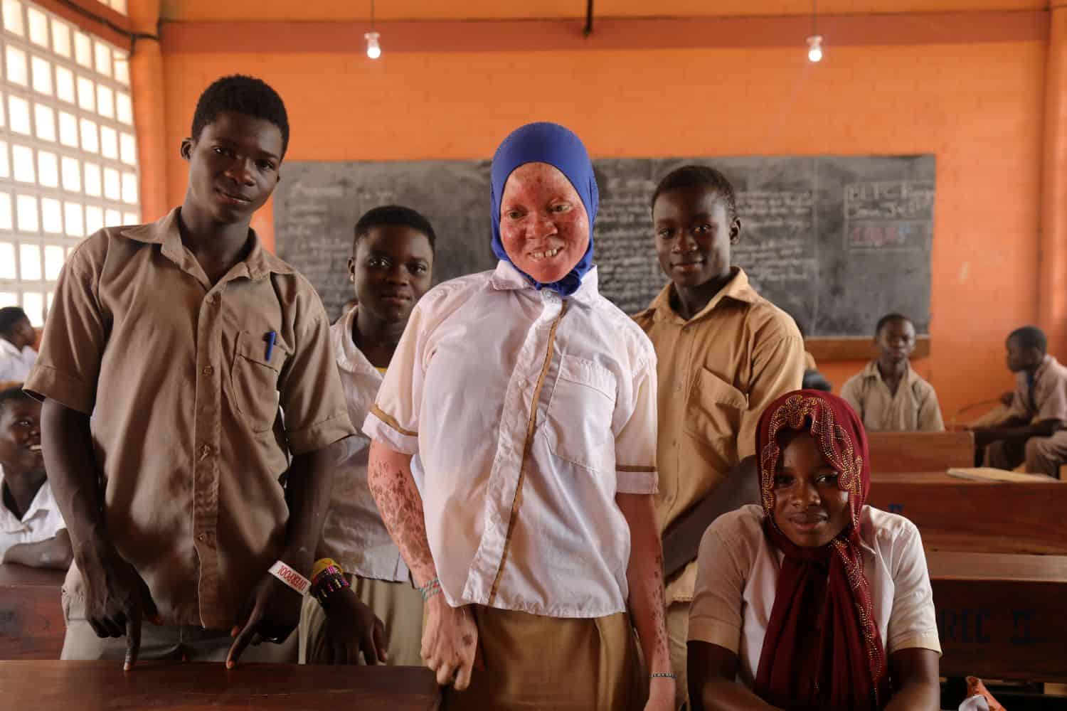 Rachidatou stands in a classroom with a group of fellow students, all smiling.