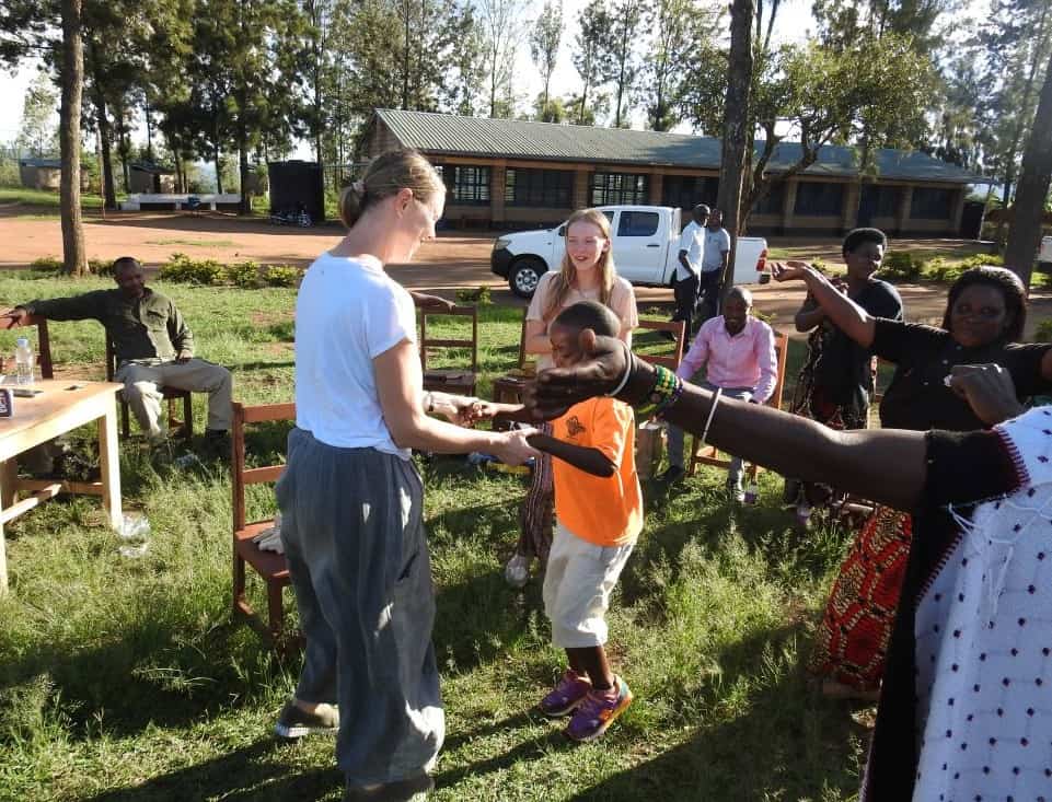 A woman wearing a white t-shirt holds hands with a boy wearing an orange t-shirt, surrounded by people celebrating outside.