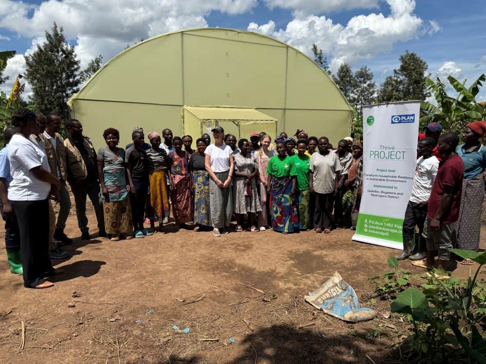 A group of people stand outside a tan structure with a sign next to it that says Thrive Project.