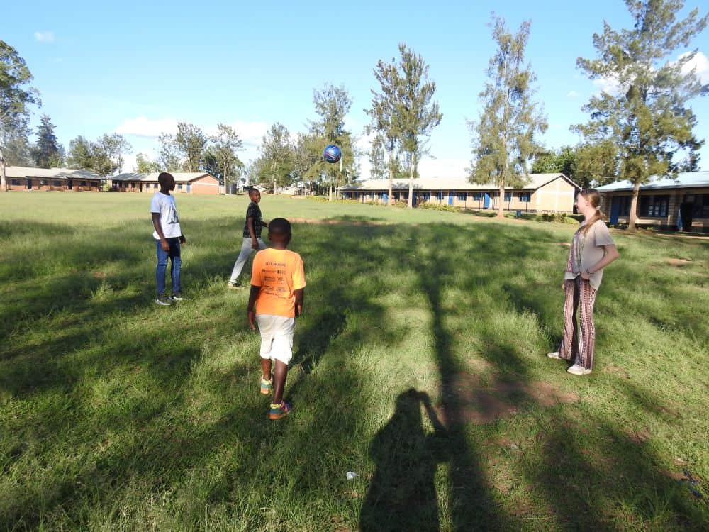 A small group of children play soccer outdoors in a large, grassy area.