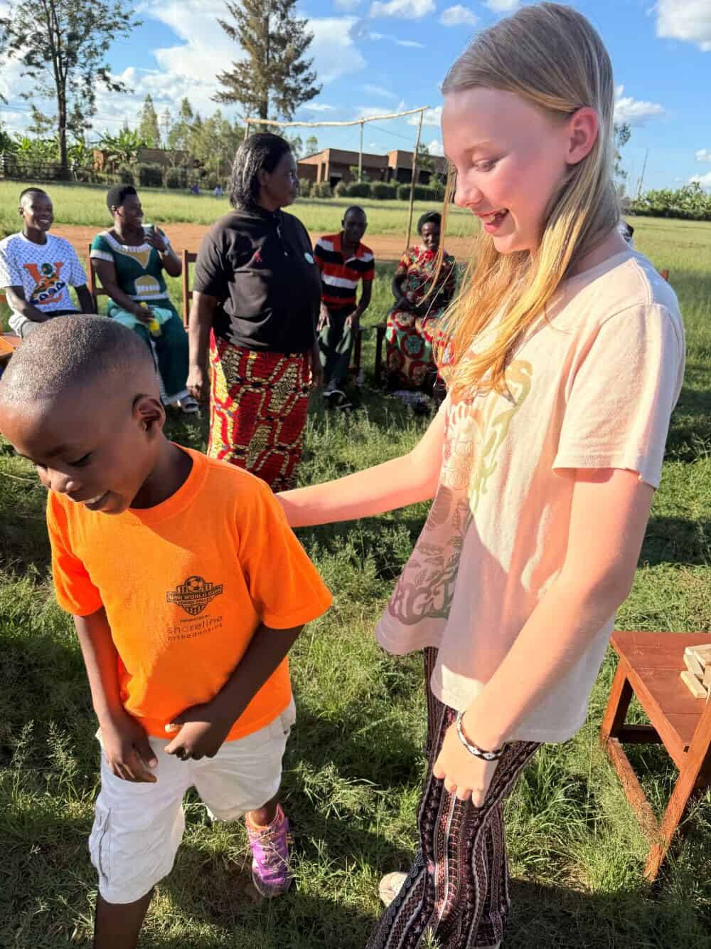 Obed, wearing an orange shirt and shorts, and Avery, wearing a pink shirt and patterned pants, smile together outside.