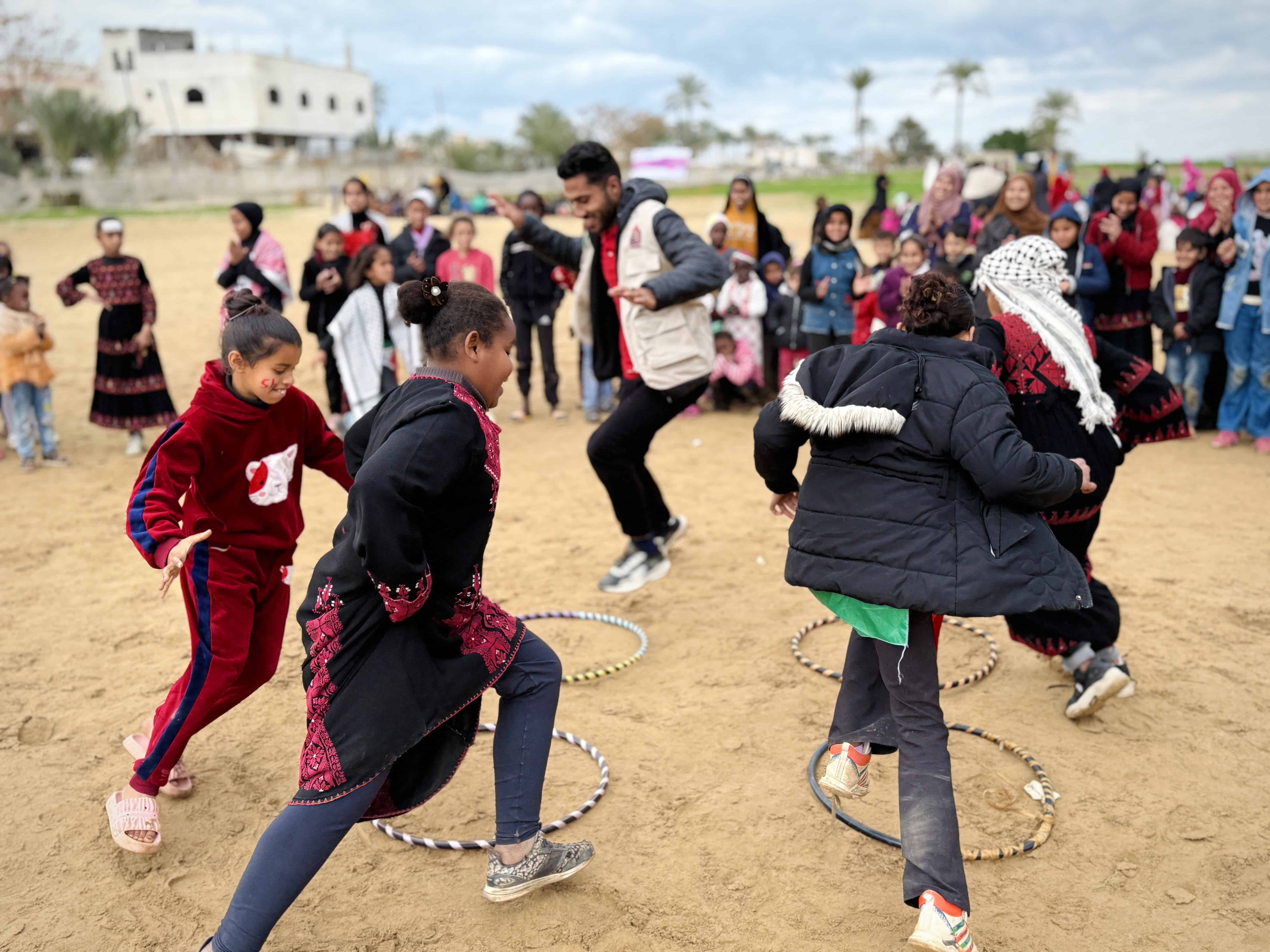 Children in Gaza play an outdoor game with hula hoops in a group activity, supported by Plan International safe spaces for displaced families.