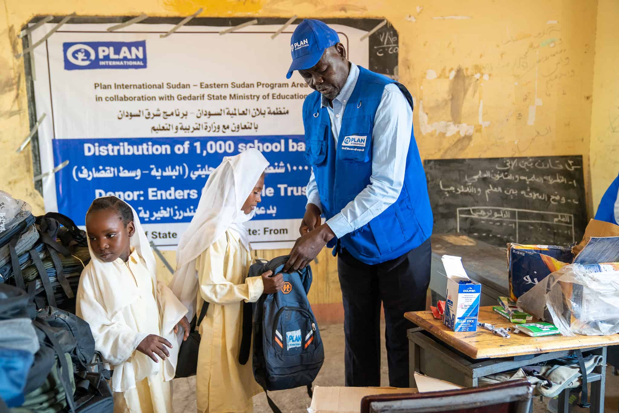 In Sudan, a Plan staff member distributes backpacks two two young girls