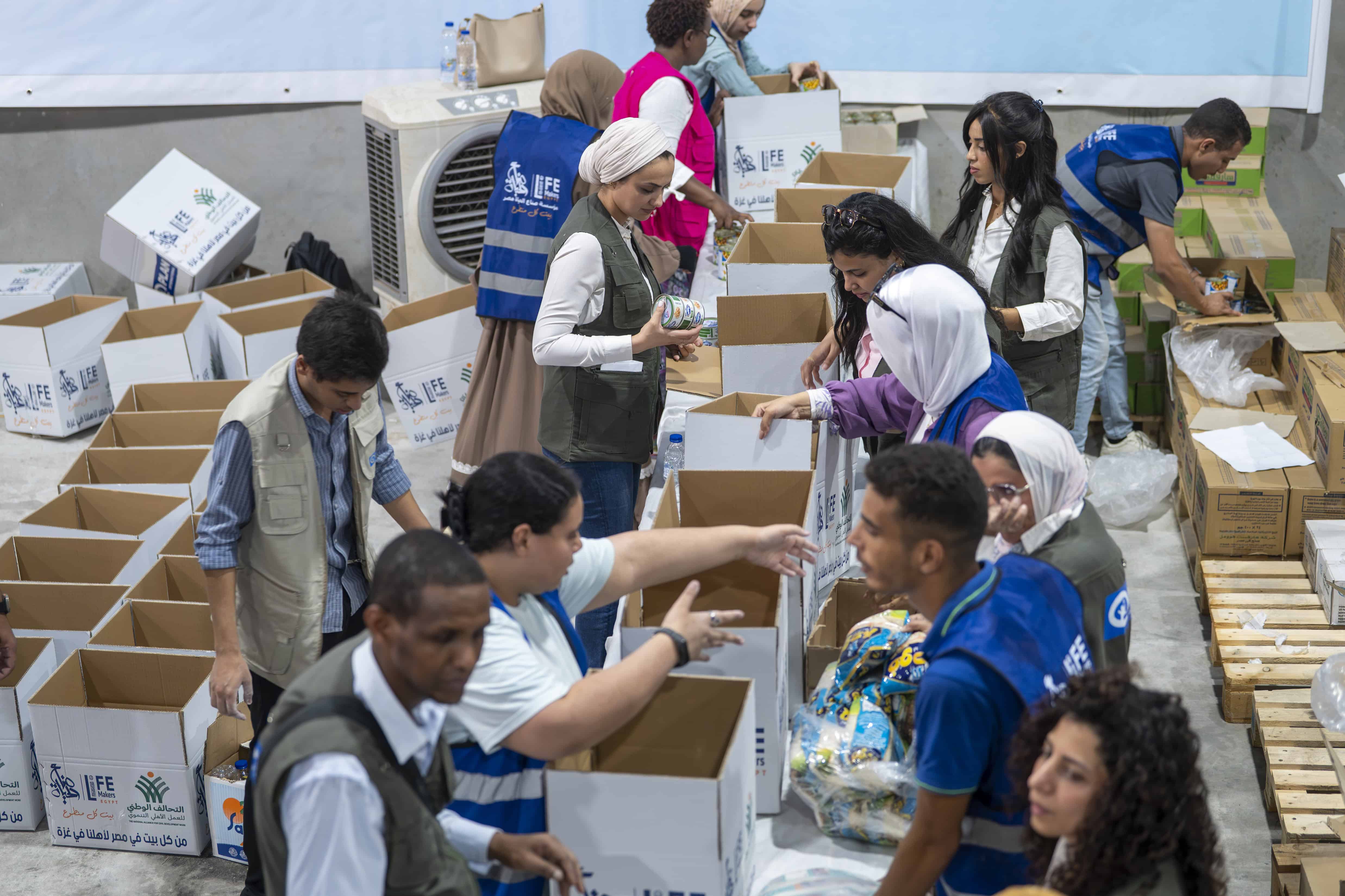 Volunteers and Plan International staff packing food parcels in a Cairo warehouse for Gaza aid convoy, working alongside Life Makers Foundation.