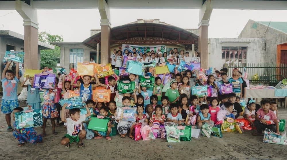 A group of children hold up the school supplies they received at the Pay It Forward event.