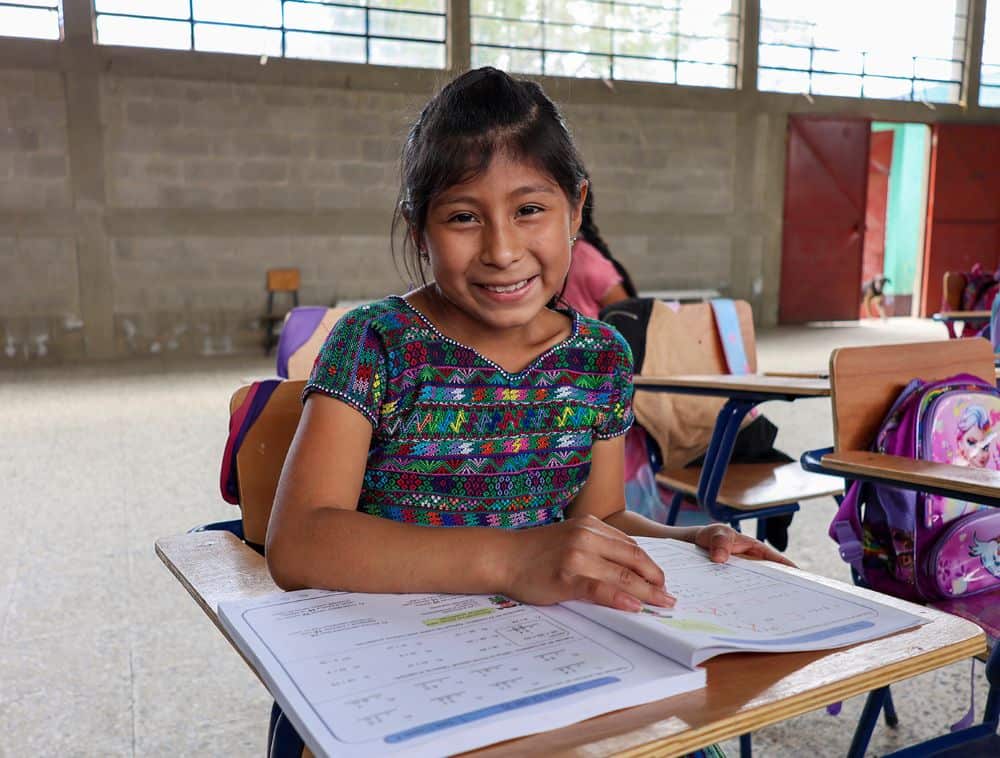 A smiling sits at a desk with a workbook open in front of her.