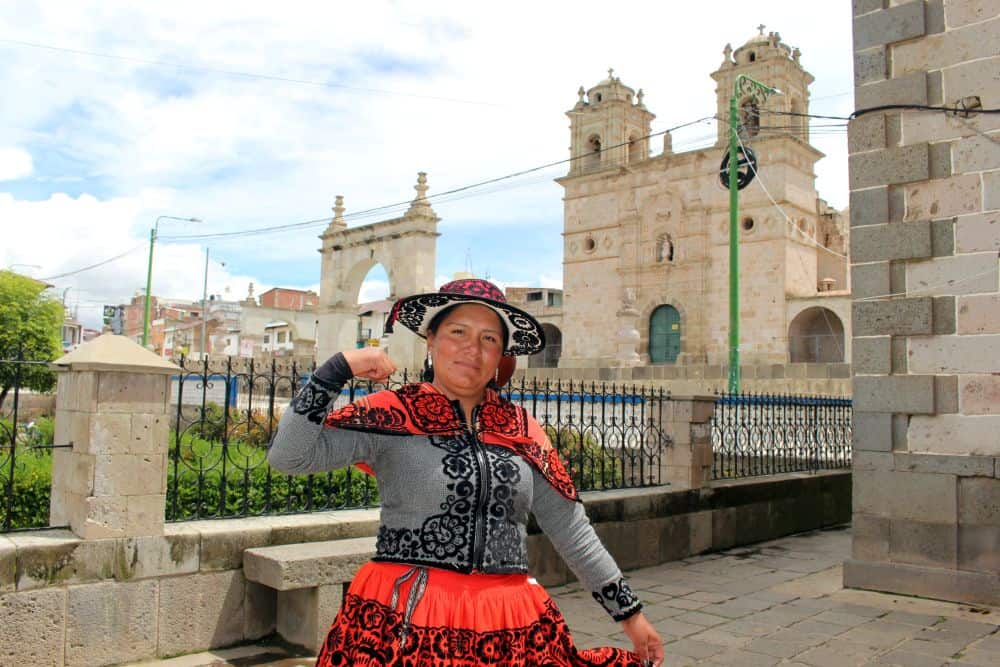 Jessica, a former sponsored child in Chumbivilcas, Peru, stands in traditional Andean clothing in front of a historic church.