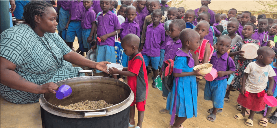 A teacher serves primary school children in Kilifi County, Kenya, as they queue to receive a meal of rice, lentils and dried vegetables through Plan International's school feeding program.