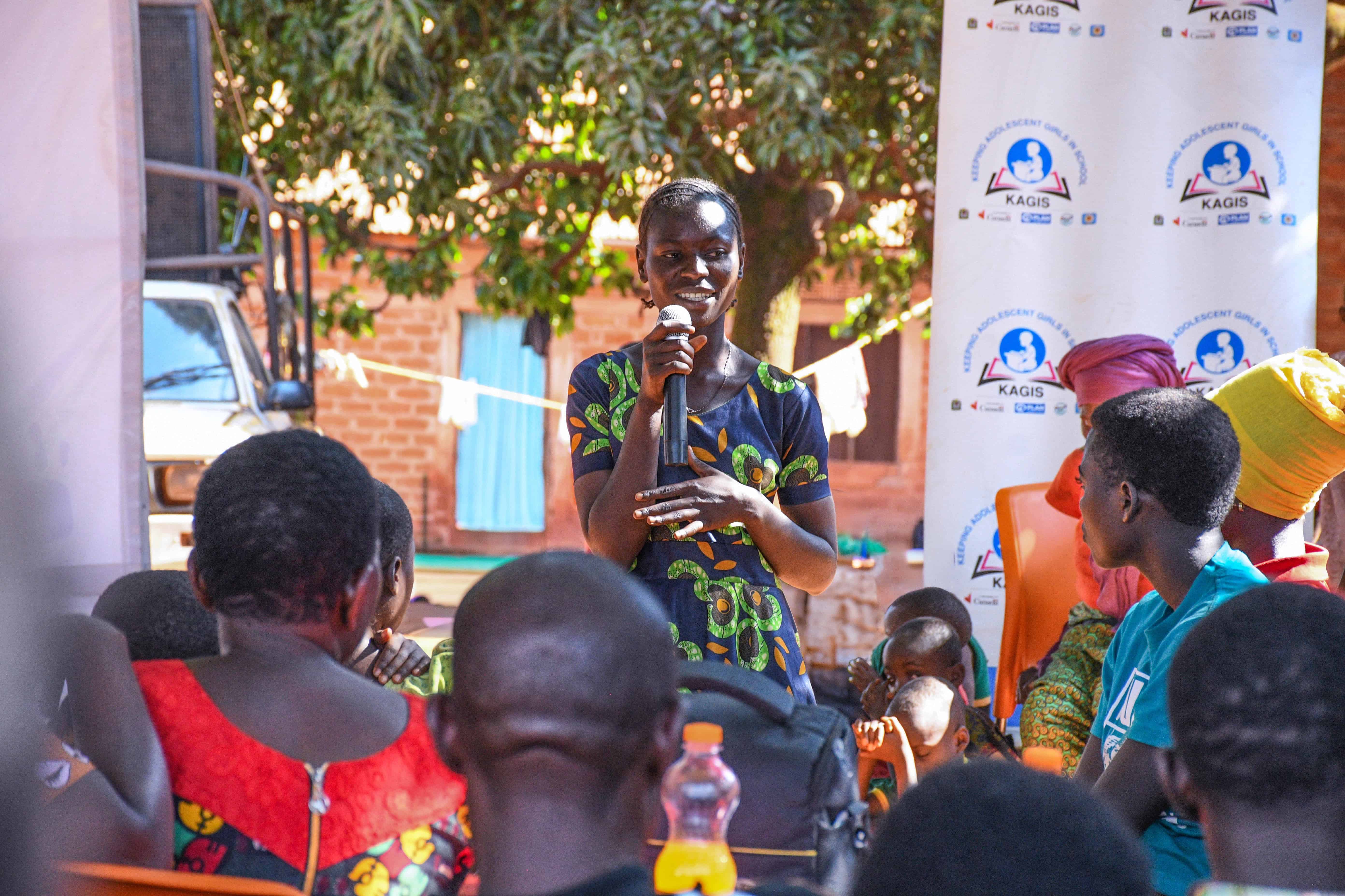 A young woman speaks to a community gathering at a KAGIS event in Tanzania.